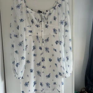 Vit klänning med blåa blommor - Klänningen är från Gina tricot och är aldrig använd. Prislapp är kvar på klänningen och klänningen har inga skador eller fläckar. Klänningen är köpt för 459kr.