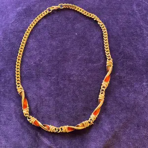 En guldfärgad halskedja med röda och orange detaljer   Okänt material 