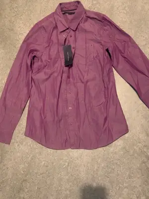 Denna lila skjorta från Tommy Hilfiger är en riktig skatt som aldrig har fått chansen att komma ut ur garderoben. Den är helt oanvänd och prislappen är fortfarande på plats Ta chansen och köp, Retur stöds dock ej köparen står för frakten (kan mötas upp)