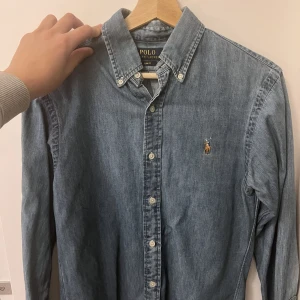 Denim Ralph Lauren Skjorta SlimFit - 1499kr Nyköp pris!  Denna skjorta är i ett jätte bra skick och har knappt använts! Den är otroligt fin och stilren men har inte passat mig i storlek, så jag säljer den nu!   Den är åtsittande och enkel att kombinera med olika plagg. Hör av er vid frågor:)