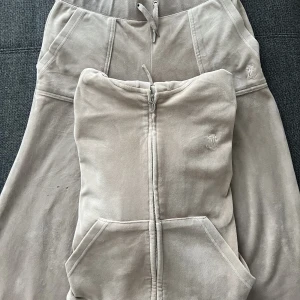 Juicy Couture  - Juicy sett i färgen beige. Använd få gånger och är i bra skick. Det saknas tre metall saker på banden framme. Koftan i storlek M byxorna i storlek S.