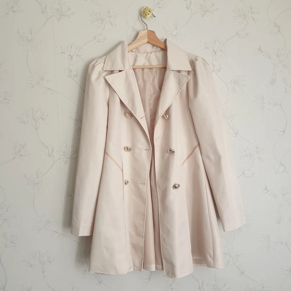 🩷FÖRST TILL KVARN!🩷 Super söt beige trenchcoat med guldfärgade knappar. Kappan har puffärmar och volanger i baksidan, fockor i fram. Dock finns en fläck i fram (tredje bild) som jag inte lyckats få bort, därav priset. Vill bli av med ASAP!. Jackor.