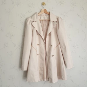 Kawaii trenchcoat beige - 🩷FÖRST TILL KVARN!🩷 Super söt beige trenchcoat med guldfärgade knappar. Kappan har puffärmar och volanger i baksidan, fockor i fram. Dock finns en fläck i fram (tredje bild) som jag inte lyckats få bort, därav priset. Vill bli av med ASAP!