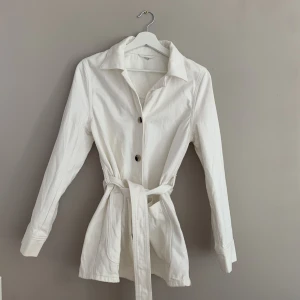 Vit jeansjacka   - Snygg vit jeansjacka med skärp i midjan. Knappt använd. 