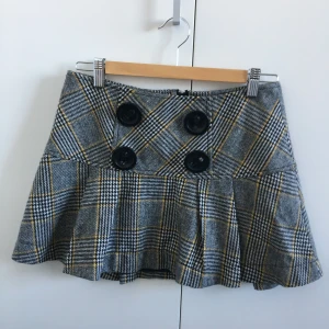 Rutig kjol, Morgan de Toi - Min systers rutiga kjol från Morgan, i jättefint skick! Veckad nertill och med dekorativa knappar, öppnas med dragkedja bak. Har ännu ett lager svart tyg under. Mått, midja: 36 cm, längd: 32,5 cm fram, 36 cm bak.