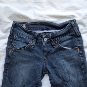 Lågmidjade jeans Lee - Lågmidjade jeans från Lee i bra skick. Rak, med något utsvängt i modellen. Färgen är lite grå/blå. Strl 27/31 Midja: 35 cm Innerbenslängd: 77 cm Ytter: 96 cm