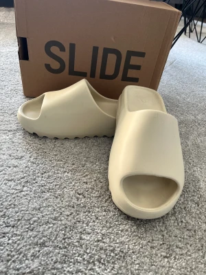 Yeezy Slide  - Hej, säljer mina Yezy Slides då dem tyvärr inte passar längre, skicket är 10/10 och är i färgen BONE WHITE Storlek 43