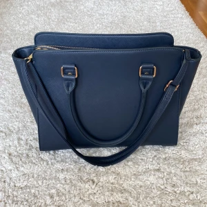 Handväska - Fin mörkblå väska med gulddetaljer i nyskick (inga defekter och knappt använd)!  Bredd: 40 cm, höjd: 30 cm💗 Skriv för fler bilder!