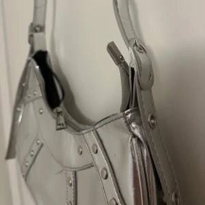 Silvrig väska - Trendig silvrig väska, nyligen köpt men aldrig använd. Ställbart band. 29 cm rakt över. 