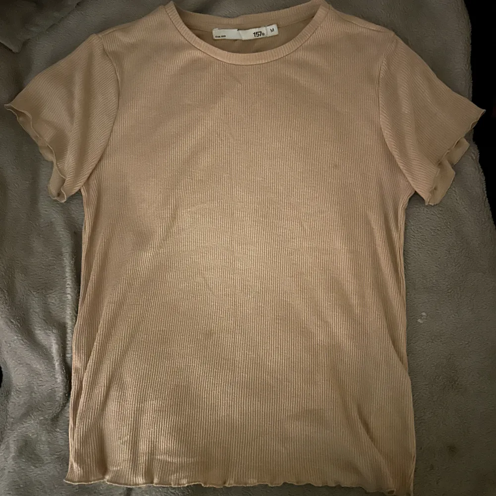 En skogsgrön t-shirt där det står ”elite” på baksidan, samt en ribbad beige t-shirt med volang vid midjan samt axlarna. 20 kr st, 30 kr tsm.. T-shirts.