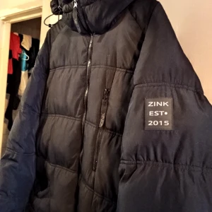 Zink long puffer jacket - En svart pufferjacka i modell längre. Alltså som en dunkappa men i syntetmaterial. Strl 44/46. Gott skick, som ny!