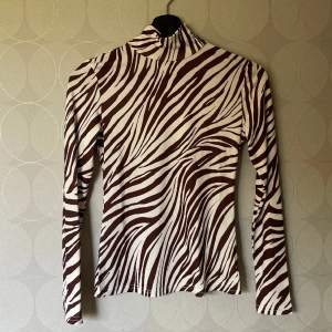 En tröja i zebramönster, färgerna brun och vit. Är väldigt skönt material, sitter tight. Fint skick!