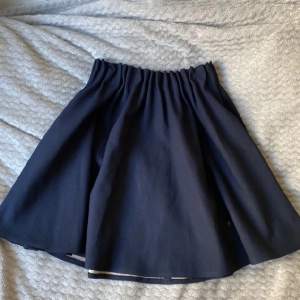 Mörkblå kjol, ”preppy”, går ut lite mer vilket gör den puffig och ger en ”prinsesslook”, ser likadan ut både fram och bak 