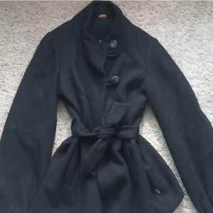 En svart kappa som har legat i garderoben, har använt en till två gånger, men den är varm och skön, har knappar som man kan stänga med samt ganska stora fickor.