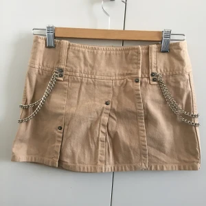 Kjol från Guess - Supercool beige kjol av bomull från Guess! Min systers, använd ett fåtal gånger, i toppskick. Det är en omlottkjol som kan knäppas upp hela vägen. Veckad framtill och med två kedjor på sidorna. Längden är 31 cm och bredden över midjan 35,5 cm.