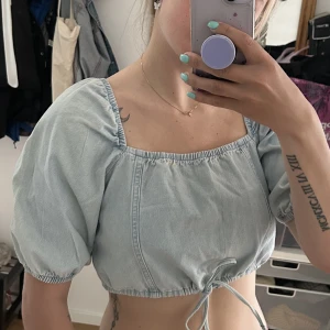 Jeans topp - Croppad topp med puffärmar i jeanstyg. Reglerbar i hur vid man vill ha den med knytband. 