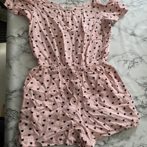 Rosa kort jumpsuit - Det är som en byxdress fast med shorts och den är rosa med svarta små hjärtan på. Väldigt fin att ha när man grillar, är i stranden eller bara är ute. 