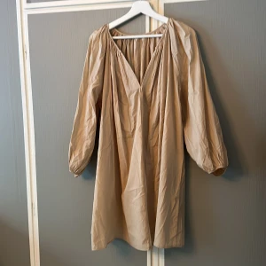 Klänning  - Beige klänning i runt material, perfekt på sommaren om man inte vill ha något varmt på sig. Även skit snygg med ett par höga stövlar till på utekvällen. Använd en gång. (Frakt tillkommer) 