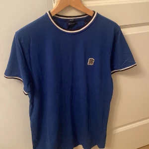 Blå Gant t-shirt - Fin och mjuk t-shirt från Gant, den har använts ett par gånger men är i fint skick. Köptes förra sommaren. Priset är 150kr men kan förhandlas ner. Storleken är L men den passar även om du vanligtvis har M som storlek men lite löst. 