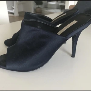 Mörkblå sandaletter skinn Stl 38 Nyskick  - Superfina högklackade sandaletter från HM Trend. Ovandel i mörkblå satin, innersula o yttersida i äkta skinn/läder. Gjorda i Portugal, premium. Stl 38, normal i Stl. Klackhöjd längst bak 10 cm.  Nypris 799:-. Använda en gång. Säljes pga benska
