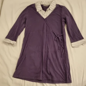Lila tunika med skjort-krage - Lila tunika med fastsydd krage och ärmändar samt knytning i höften. Ser ut som omlott med är fastsytt. Fin och bekväm! Hör av dig för mer info/fler bilder!