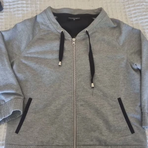 Jack/sweatshirt  - Grå jack/tröja modell med svarta detaljer vid fickorna och svart mesh tyg ryggen.  Mudd nertill och i ärmar. Nästintill oanvänd 