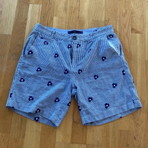 Shorts i linne från Suit - Lätta sköna shorts från märket Suit i storlek 32/M. Materialet är linne och väldigt lätt och svalt. Broderade blommor. Färgen är randig med blått och vitt. Perfekta till en riktig varm sommardag. 