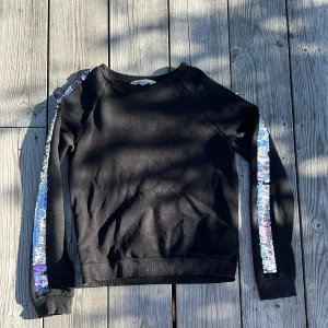 Svart tröja med paljetter - En svart basis tröja med glitter på armarna. Det går att skifta mellan lila/rosa/blå och silver.💖 Har låsnat någon tråd vänster arm och har en liten fläck på höger arm men annars är den i bra skick. Storlek 146/ 152. Köpt från HM Pris 60kr. 