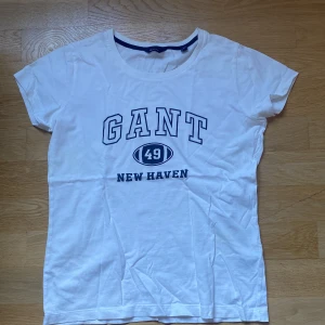 Gant T-shirt - Vit Gant t-shirt i fint skick, nästan oanvänd men hyfsat gammal. På sidan ligger en liten gul/ grön fläck som nästan inte alls syns om man inte håller upp mot starkt ljus.