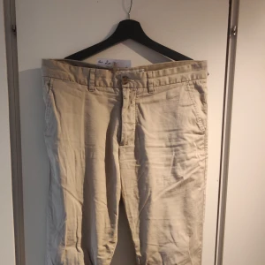 Chinos - Beige - Selected Homme  - Säljer ett par sjukt sköna chinos från Selected Homme för att de ej används. Sytt på en knapp som lossnade i gylfen men inget som syns när man har dem på (täcks av skärpet). Nypris ca 400 kr
