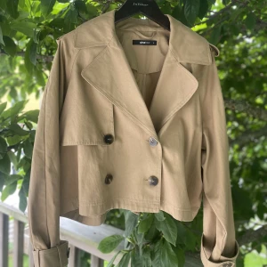 Kort trench/kappa - Säljer min fina korta trenchcoat/kappa från GinaTricot, då jag tyvärr inte får någon användning för den. Den är i utmärkt skick, använd max 3 gånger. Storlek S, men lite större i modellen. Köpt för 599 kr. 