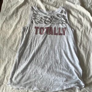 Linne med TOTALLY text  - Ett grått linne med texten TOTALLY på av rosa paljetter.Perfekt till sommaren ⭐️🤙💕🩶