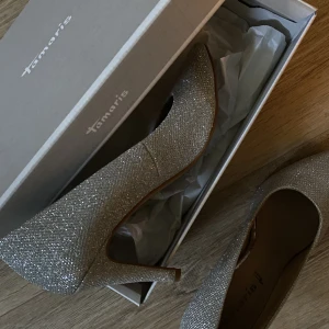 Silver glam pumps från Tamaris - Ett par silver glittriga klackskor (pumps) från märket Tamaris som är köpta genom Zalando. Relativt höga klackar som enbart använts en gång. Använde dem på min bal i gymnasiet och behöver dem ej längre. Väldigt bra skick🩶