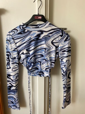 Blå topp - Oanvänd blå mönstrad topp med knytning i sidorna. Stretchigt material så passar XS-M