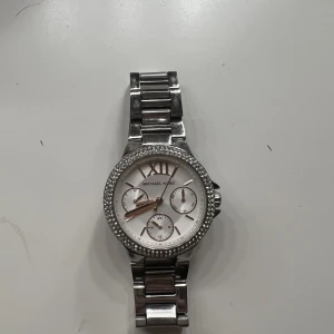 Michael kors klocka - En jättefin Michael Kors klocka i silver med stenar på. Är köpt i höstas men knappt använd. Väldigt bra skick! Alla stenar sitter på och det är inga större repor. Spännet fungerar precis som det ska. Nypris låg på 3000kr