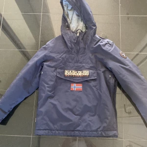 Napapijri vinterjacka - Bekväm vinterjacka som knappt är använd. Fleece inuti och varm till vintern. Dragkedja vid halsen, vid vänster sida och en stor ficka på magen. Färgen är nöstan mörkblå.  Storlek L 