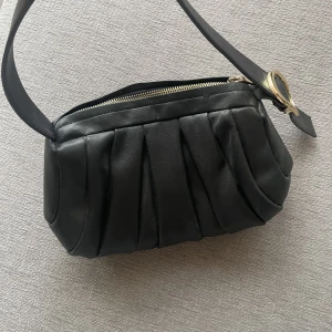 Axelremsväska  - En axelremsväska med puffigt stuk och gulddetaljer