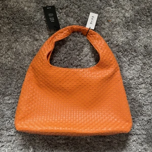 Ny NA-KD orange vävd väska - Säljer denna fina nya oanvända vävda väskan från NA-KD i orange. Väskan är ganska stor, tredje bilden visar den på axeln. Nypris är 499kr! Säljer för 300kr med frakten inkluderad.