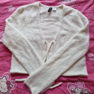 Kofta med knytdetalj - Fluffig vit kofta i croppad modell, knyts i fram. Sparsamt använd i väldigt fint skick🌸 Fin över klänning eller som en topp med ett par jeans😊 Figurnära modell, storlek m