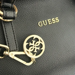 Guess väska - En äkta väska från guess som är köpt från guess butiken. 4 fack varav två med dragkedja. Långt band med guessmärket på medföljer. Använd få gånger. Stor och rymlig i svart läder. Gulddetaljer