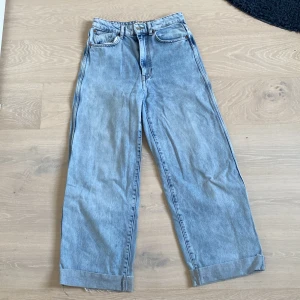 Ljusblåa vida högmidjade denimbyxor  - OBS lite slitna längst ner på höger byxben, men annars i ganska bra skick. Jag vikte längst ner på byxorna själv för dom var för långa på mig. Rekommenderar att inte ta bort det för det är just där det är slitet. 