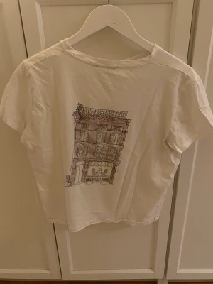 Tshirt - Vit shirt med tryck på ryggen, går att ha tshirten åt båda hållen. Storlek xs men passar S/M