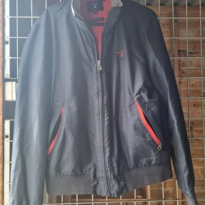 Gant jacka - Svart/blå jacka med röda detaljer. Använd men i fint skick bortsett från en repa på ryggen.