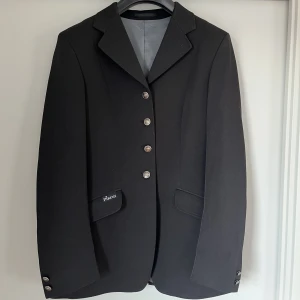 Pikeur svart tävlingskavaj - Superfin klassisk svart tävlingskavaj från Pikeur i modellen Epsom. Nyskick då den enbart använts 1-2 gånger. Storlek 76 i Pikeurs egna storlek, passar en storlek small.