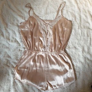 Jumpsuit / playsuit / romper i satin - Ett underklädesplagg i lätt silkigt tyg bestående av 92% polyester och 8% elastin. Använd men övrigt i bra skick. Spets och knappar. Midja i stretch. Banden går att justera.