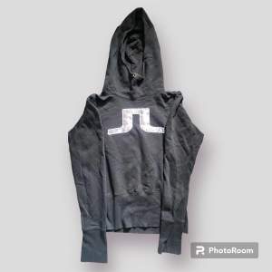 J.Lindeberg hoodie som är svart och trycket är grått och glänsande. Hög krage. Storlek L men mer som en S.
