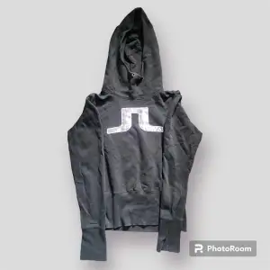 J.Lindeberg hoodie som är svart och trycket är grått och glänsande. Hög krage. Storlek L men mer som en S.