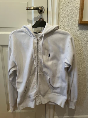 Vit Ralph lauren zip hoodie - En Ralph lauren hoodie i bra skick, inga skavanker köpt på Zalando för 1300kr säljes pågrund av att jag rensar ur garderoben. Obs! Dåligt ljus därav ser hoodie grå ut men den är helt krit vit.