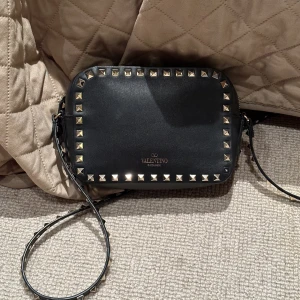 Valentino väska  - Valentino rockstud väska, svart och guld detaljer. Använd sparsamt, i fint skick! Trillat av en stud som syns på bild två. I övrigt fint skick, lite små ytliga repor finns som syns om man kikar i vissa ljus. Inget man ser annars. 