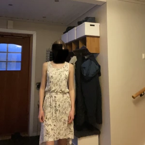 Vit klänning  - En vit tricåklänning med mönster av blad och växter från h&m🤍Den har ett midjeband med rosetter på vardera sida och är längre där bak. Använd ca 4 gånger och har inga fel.🙌🏼Strl. 170 men kan vara en XS.